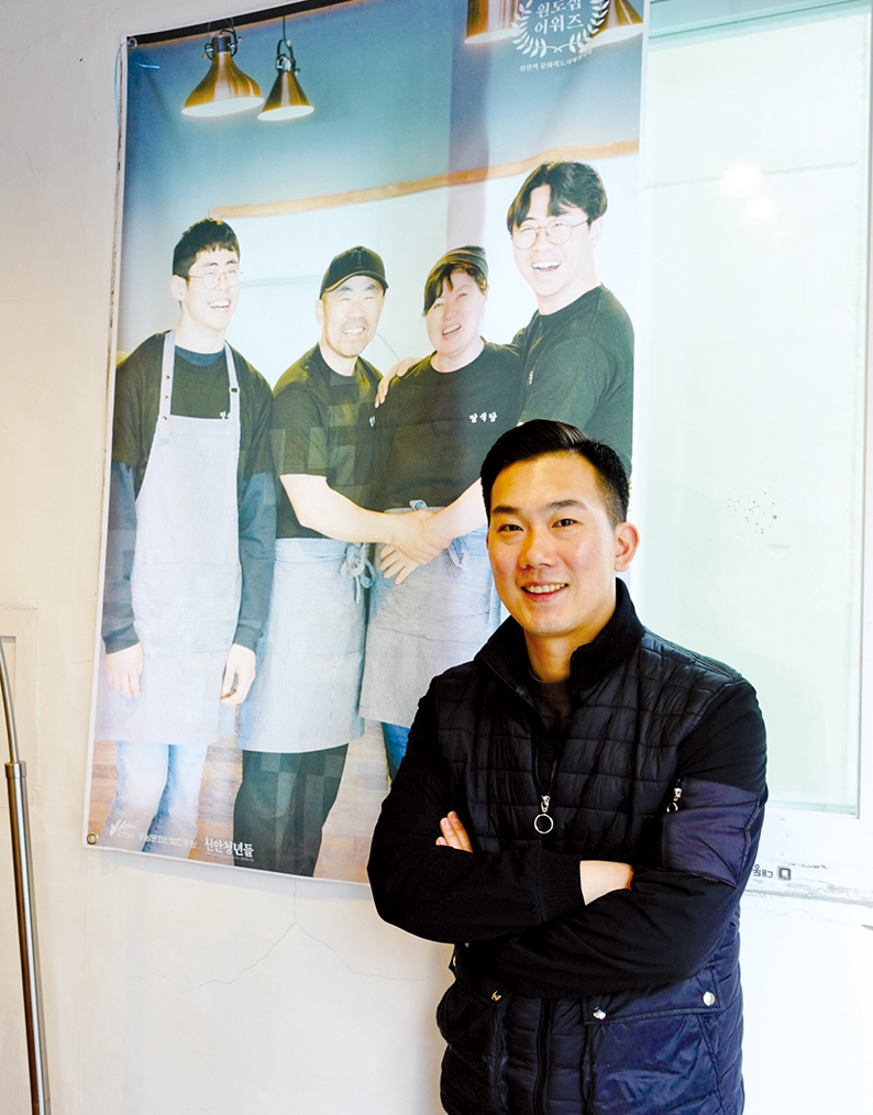 최광운 대표. 천안역 원도심 재생에 참여한 상인들의 사진을 배경으로 환하게 웃고 있다.