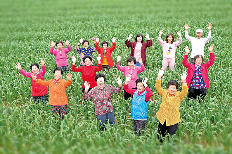 회춘유랑단 단원들이 마을 논을 배경으로 환하게 웃고 있다. 사진/회춘유랑단 제공
