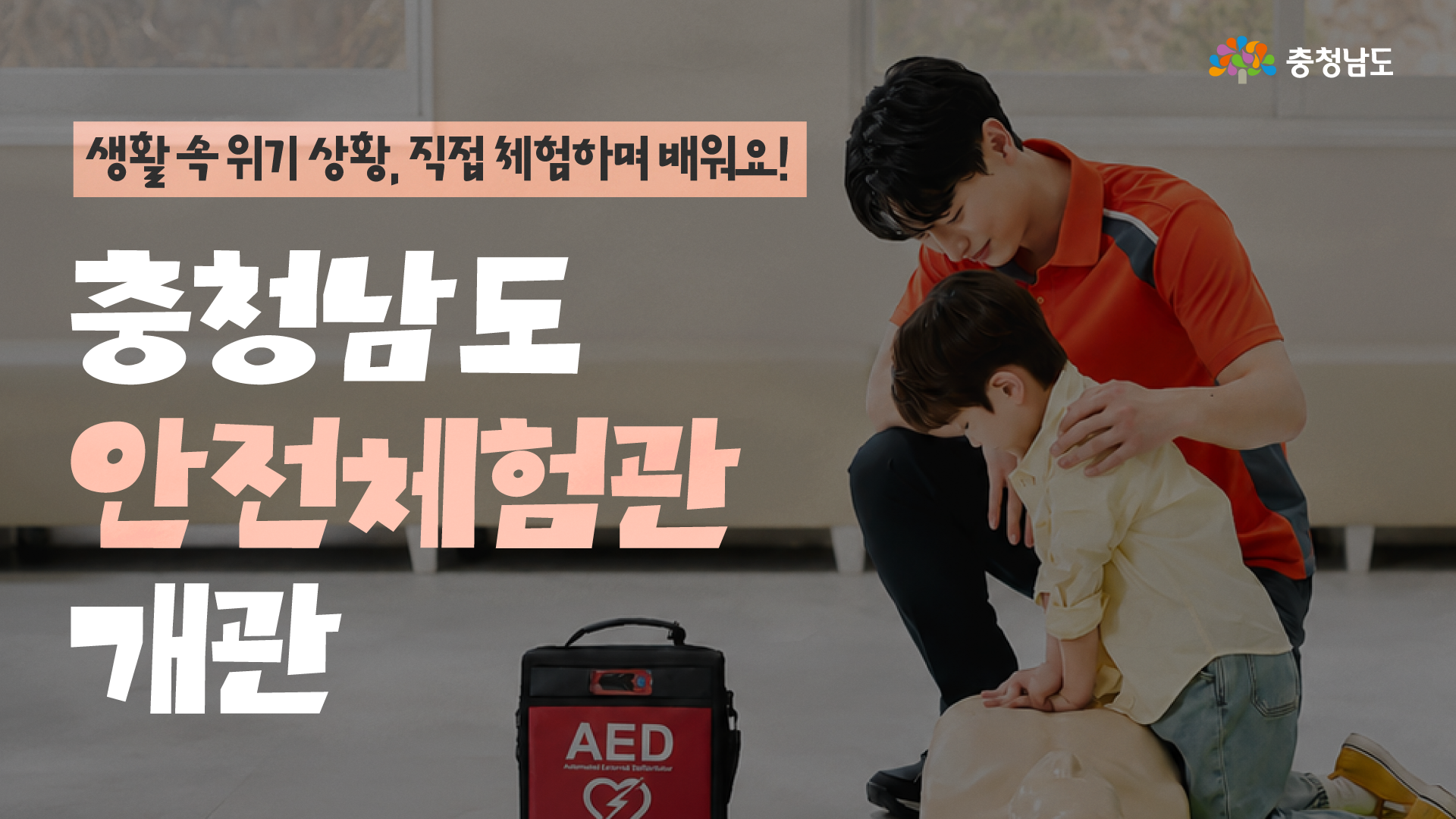 생활 속 위기 상황을 직접 체험하며 배우는 &lsquo;충청남도 안전체험관 개관&rsquo;을 알리는 가로형 홍보 이미지입니다. 오른쪽에는 한 사람이 어린이와 함께 심폐소생술 교육용 마네킹으로 응급처치를 연습하는 모습과 빨간색 자동심장충격기(AED)가 보이고, 왼쪽에는 &lsquo;생활 속 위기 상황, 직접 체험하며 배워요! 충청남도 안전체험관 개관&rsquo;이라는 제목이 크게 배치되어 있습니다. 오른쪽 위에는 충청남도 로고가 표시되어 있습니다.