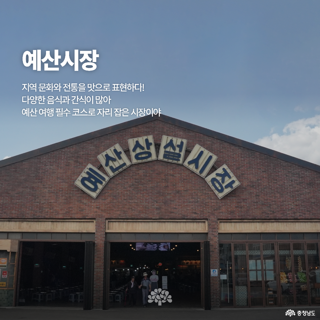 붉은 벽돌로 된 예산 상설시장 건물이 큼직한 간판과 함께 보입니다. 건물 안은 식당과 상점들이 조명 아래 활기차게 운영되고 있습니다. 시장 앞에는 방문객들이 모여 있는 모습이 보입니다.