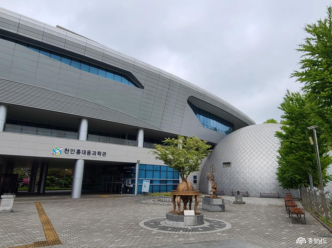 홍대용과학관 건물 외부 전경. 커다란 회색 현대식 건물로, 왼쪽엔 천문대처럼 생긴 돔 구조가 보이고 그 앞으로 벤치와 천문 관측 기구들이 배치되어 있습니다.