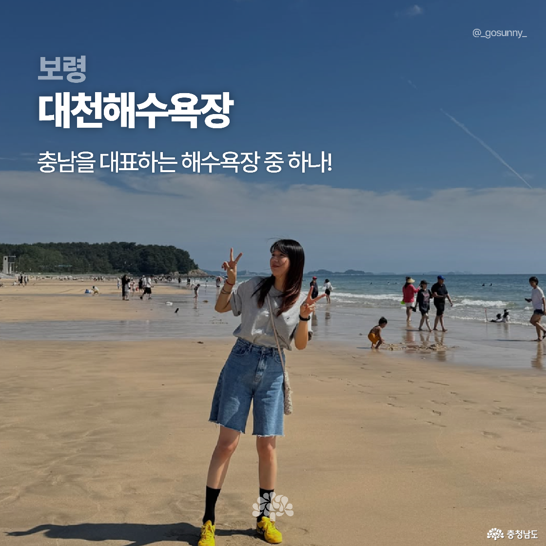 보령 대천해수욕장에서 한 여성이 손가락으로 브이를 하며 사진을 찍고 있습니다. 맑은 하늘 아래 많은 사람들이 해수욕과 산책을 즐기고 있습니다. ‘충남을 대표하는 해수욕장 중 하나’라는 설명이 포함되어 있습니다.