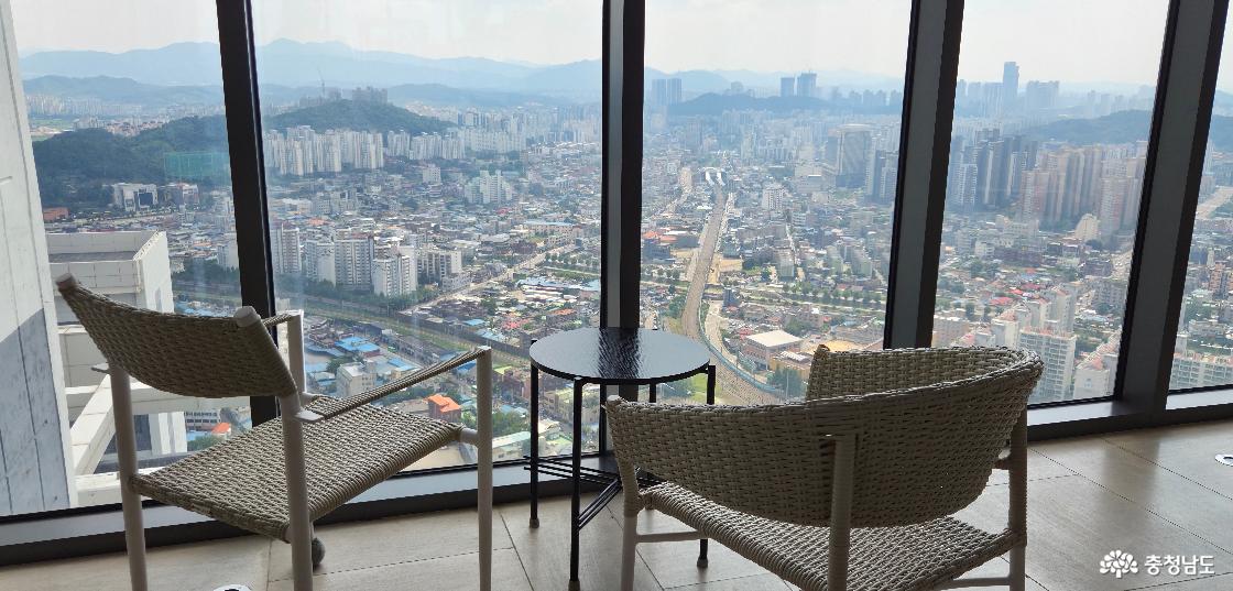 통유리창 너머로 천안 도시 전경이 보이고, 그 바로 앞에 창가석이 있어요. 테이블과 의자.