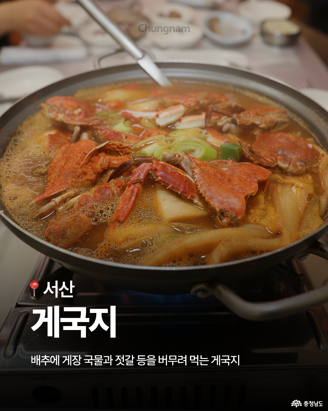 커다란 냄비 안에서 붉은 국물이 자글자글 끓고 있으며, 속에는 꽃게, 배추, 파, 무 등이 듬뿍 들어 있습니다. 식탁 위에 놓인 불판에서 김이 피어오르고, “서산 계국지 – 배추에 계장 국물과 젓갈 등을 버무려 먹는 계국지”라는 문구가 아래쪽에 보입니다. 국물의 깊은 색감과 김이 어우러져 따뜻한 한 끼의 느낌을 전하는 음식 사진입니다.