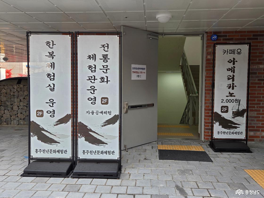 체험관 입구에는 한복 체험실 운영과 전통문화체험관운영(자율공예체험), 카페유 운영(아메리카노 2,000원)을 안내하는 배너들이 나란히 서 있습니다. 