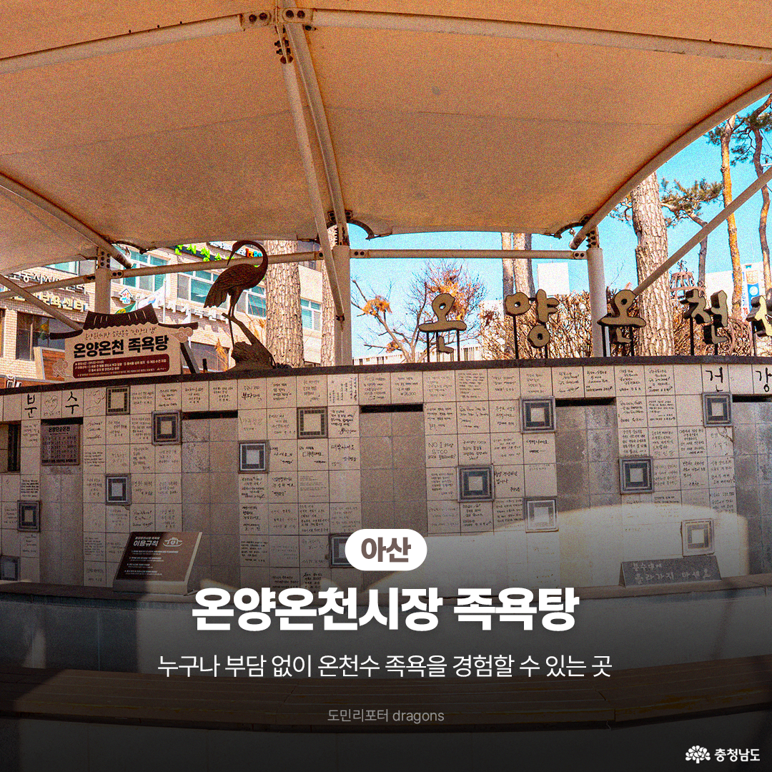 &lsquo;아산 온양온천시장 족욕탕&rsquo;의 모습으로, 야외에 마련된 족욕 시설의 타일 벽면에는 방문객들의 메시지가 적혀 있고 햇살이 따뜻하게 비칩니다. 시장 한가운데 위치하여 누구나 부담 없이 온천수 족욕을 경험할 수 있는 힐링 공간임을 안내하고 있습니다.