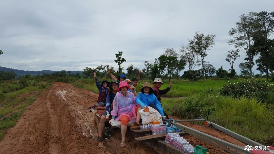 해외 봉사 현장에서 자원봉사자들이 진흙길을 달리는 트랙터에 올라 서로 손을 흔들며 웃고 있다