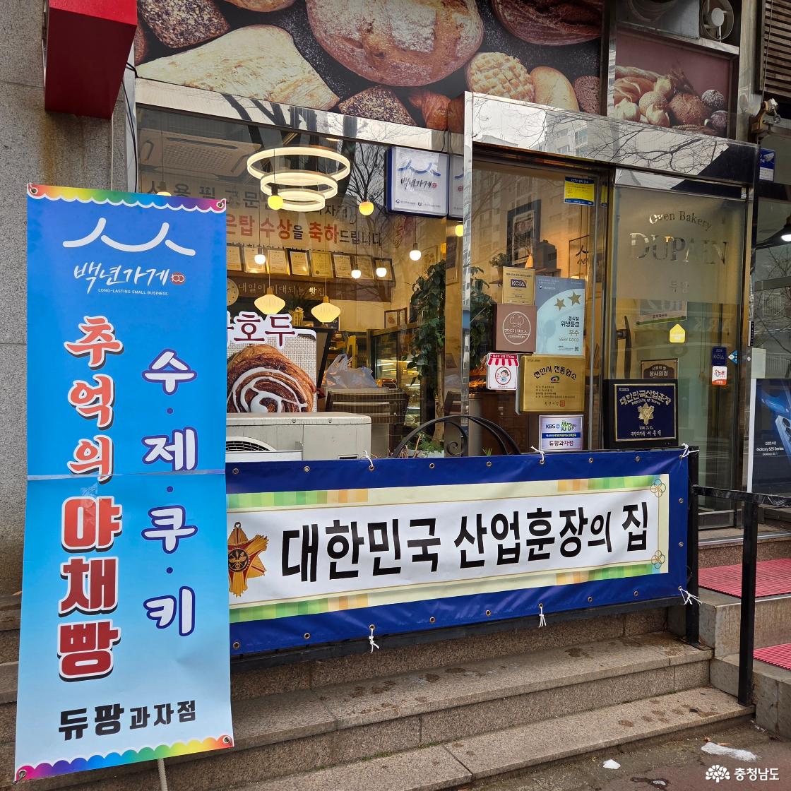 듀팡과자점 매장 외부에 백년가게(추억의야채빵, 수제쿠키) 배너와, 대한민국 산업훈장의 집 플랜카드, 위생등급 우수, 천안시 전통업소 등이 게시되어 있는 모습.