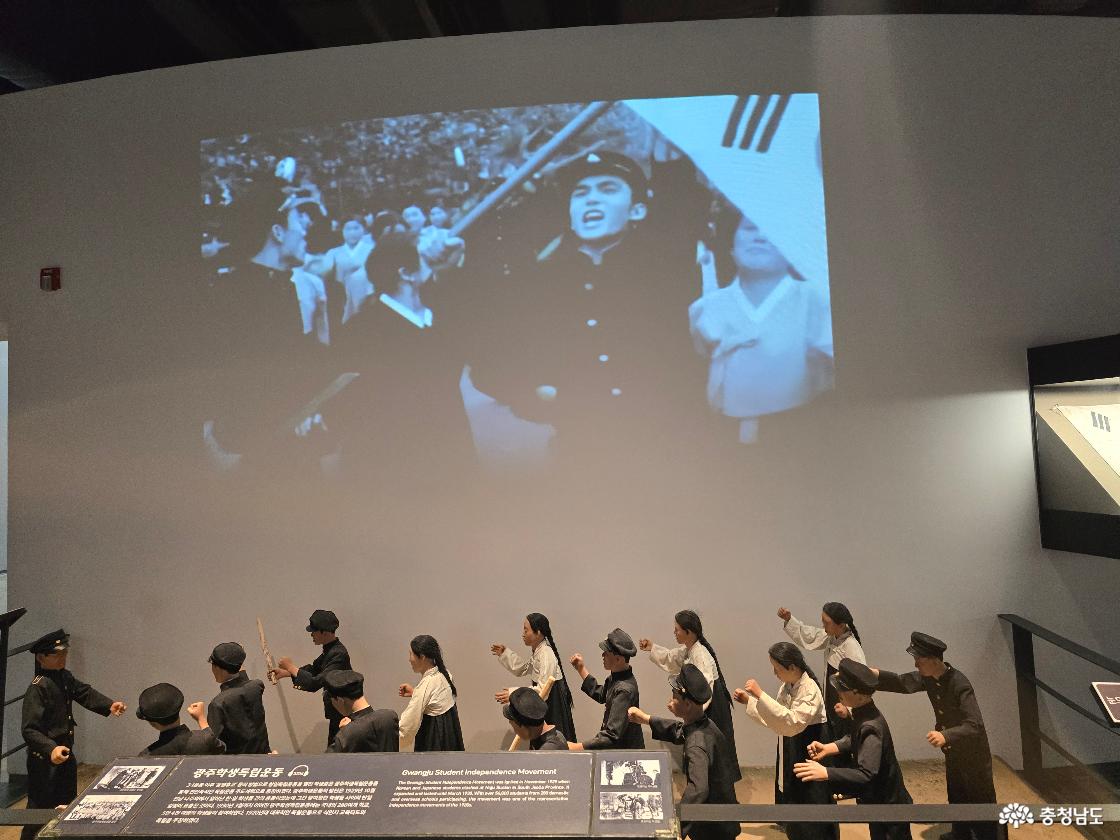 태극기를 들고 행진하는 학생 독립운동 모형과 상단에 상영되는 흑백 영상 장면