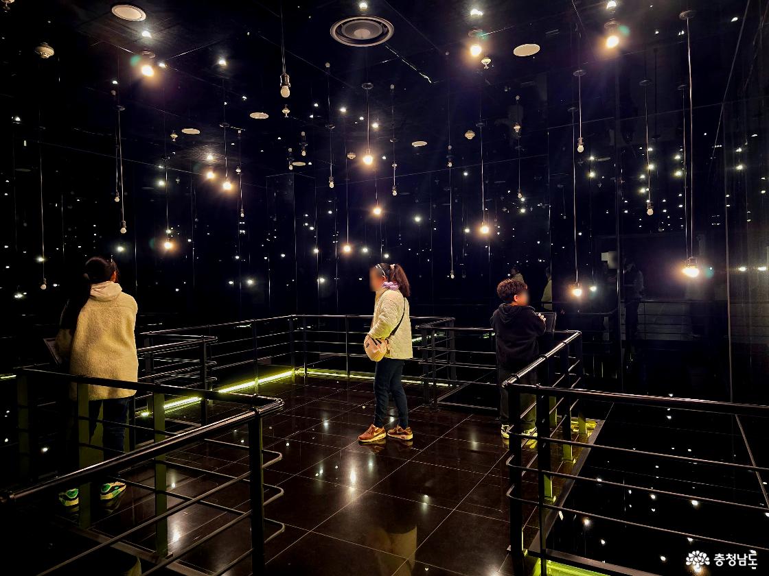 어두운 전시실에서 조명이 별처럼 빛나는 체험형 미디어 공간과 관람객 모습