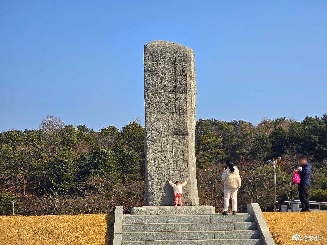 잔디 언덕 위에 세워진 광개토대왕릉비와 광개토대왕릉비를 바라보는 가족 모습