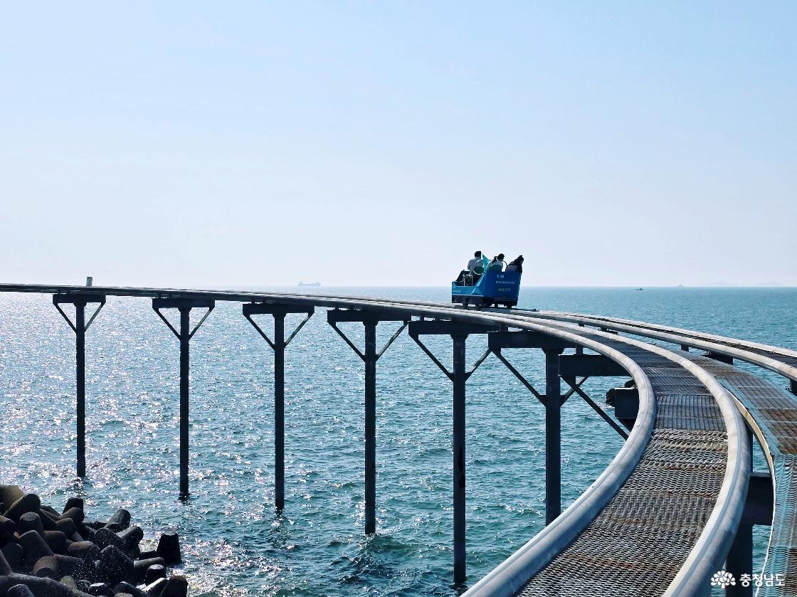 곡선 구간을 도는 스카이바이크와 잔잔한 바다, 햇살에 빛나는 물결이 인상적인 장면