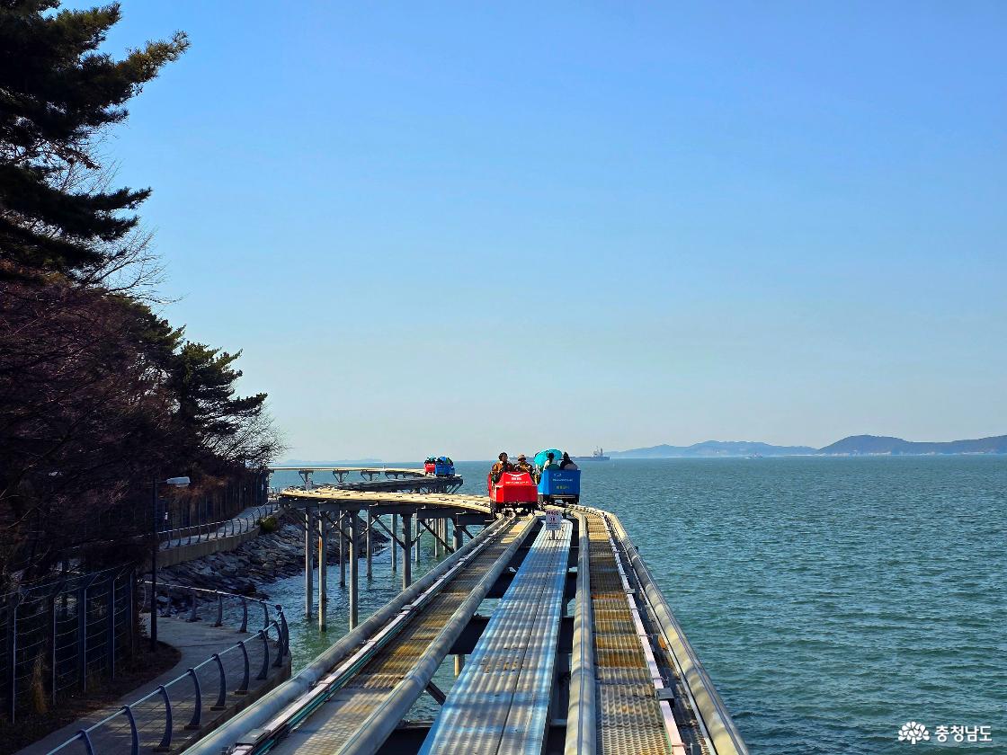 곡선 레일을 따라 달리는 스카이바이크, 바다 위 기둥 구조와 반짝이는 수면이 돋보이는 장면