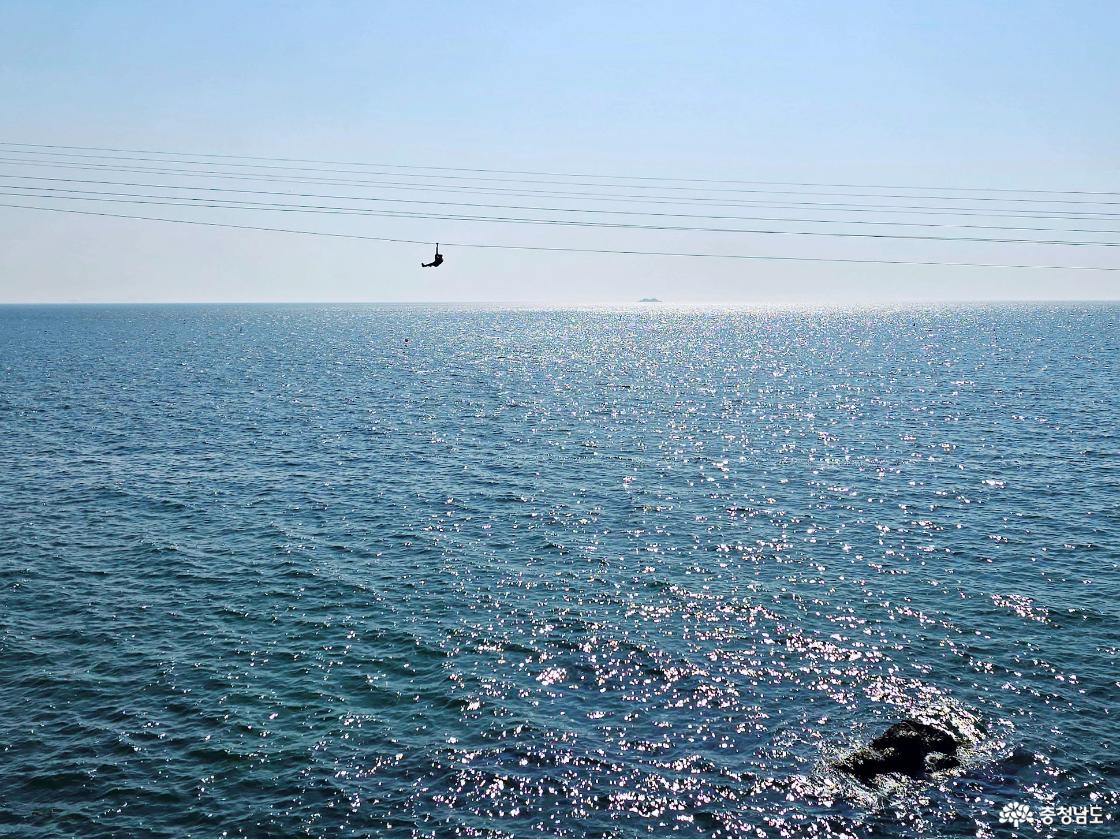 바다 위를 가로지르는 집라인 체험 장면, 푸른 수평선과 반짝이는 바다를 배경으로 이동하는 모습