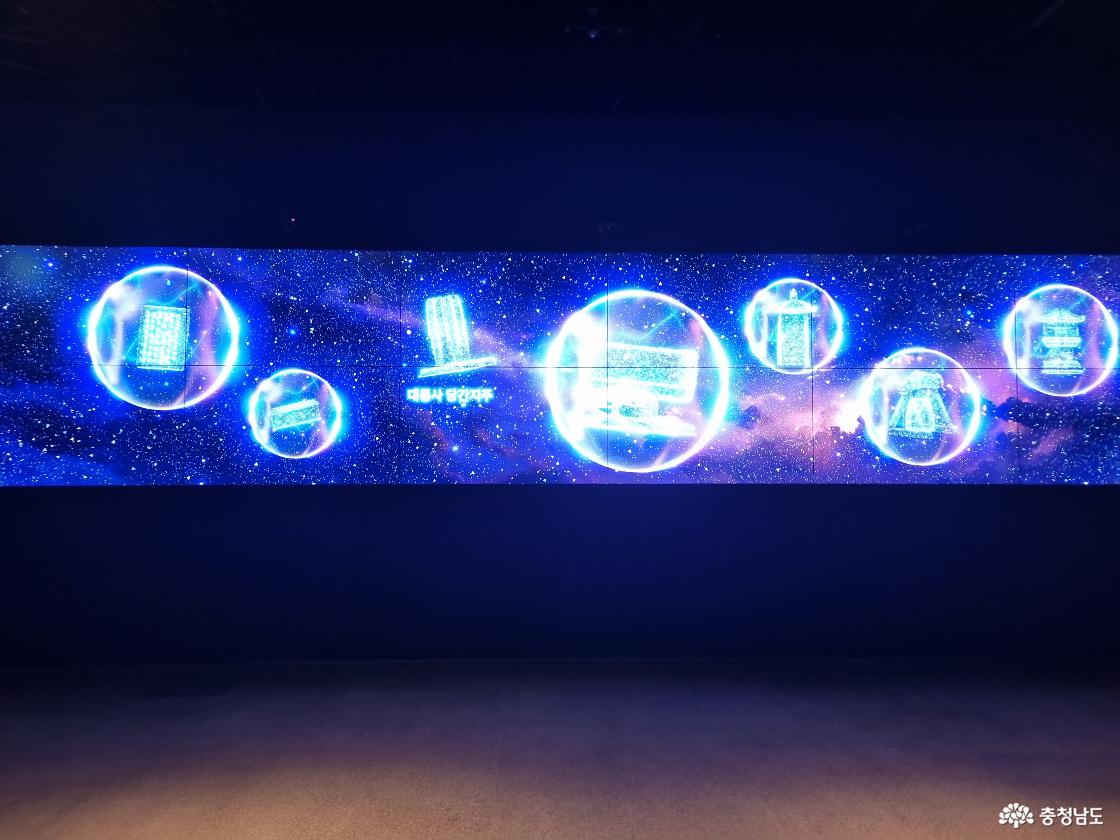 백제 유물을 우주 공간 속 빛의 구슬 형태로 표현한 대형 미디어아트 전시 화면