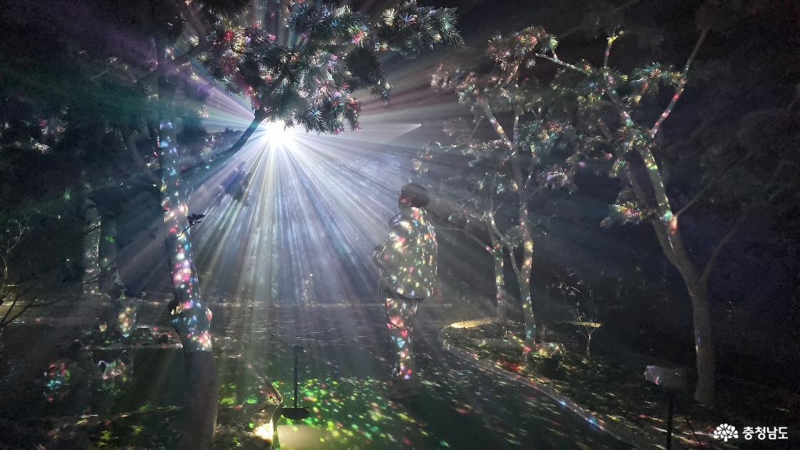 빛이 퍼지는 어두운 공간 속 길을 걸어가는 관람객 모습