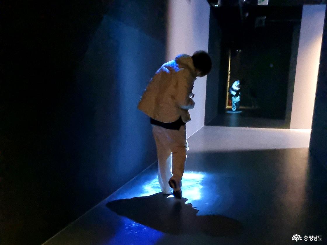어두운 전시 통로에서 빛을 따라 걷는 관람객 모습