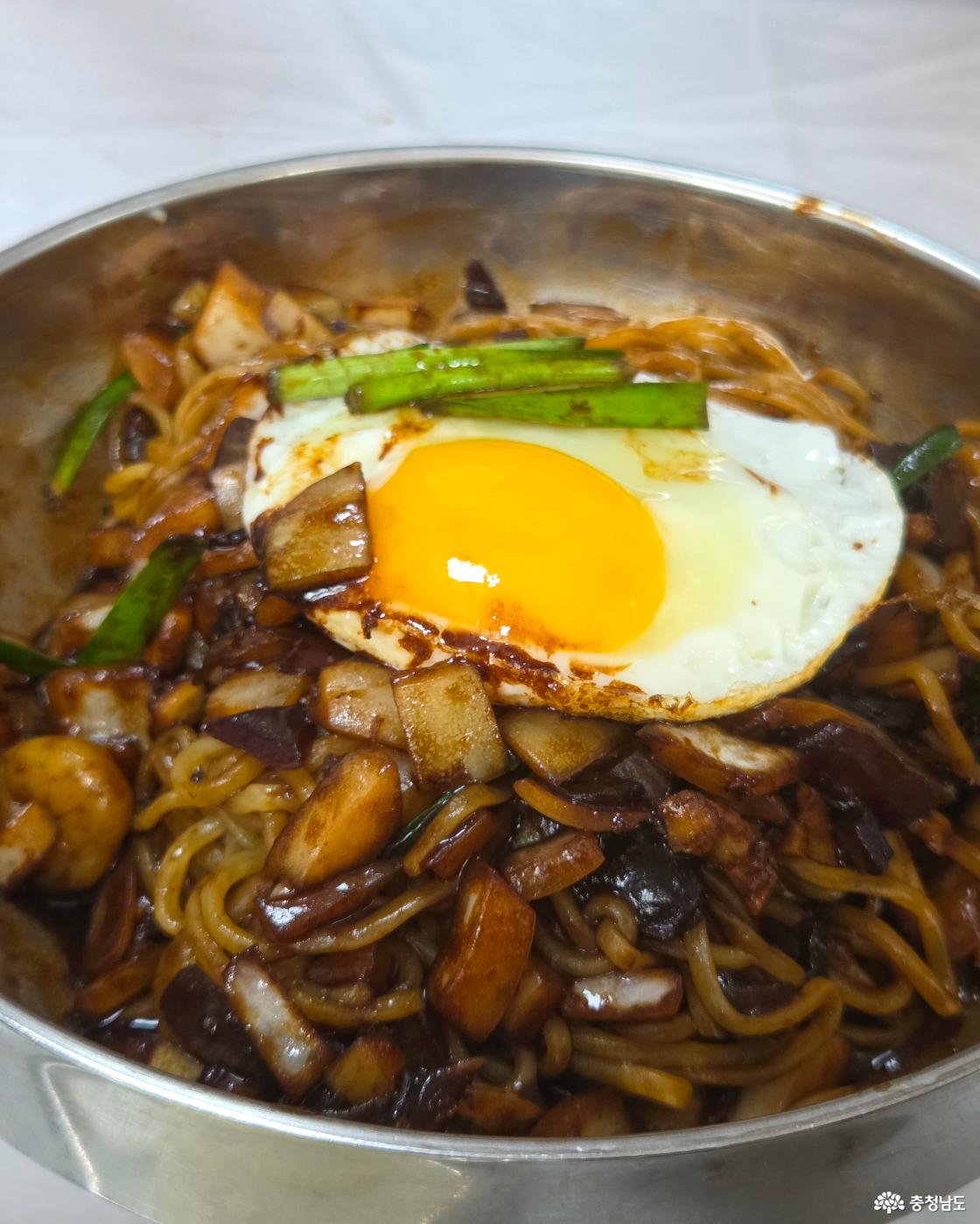 먹음직스럽게 잘 비벼진 간짜장 위에 노란 노른자가 살아있는 반숙 계란후라이와 초록색 부추가 올라가 있습니다. 