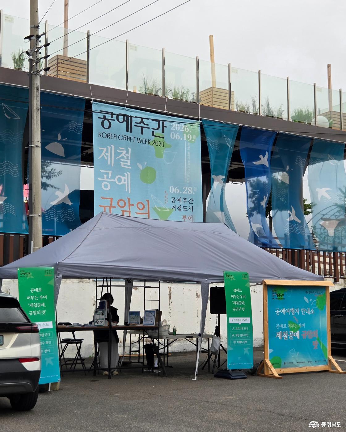 2026 공예주간을 알리는 현수막이 크게 걸린 123사비 아트박스 아래에 마련된 종합안내소가 있습니다. 종합안내소 부스 앞에는 '공예여행자 안내소'라고 적힌 하늘색 입간판이 방문객들을 맞이하고 있습니다.