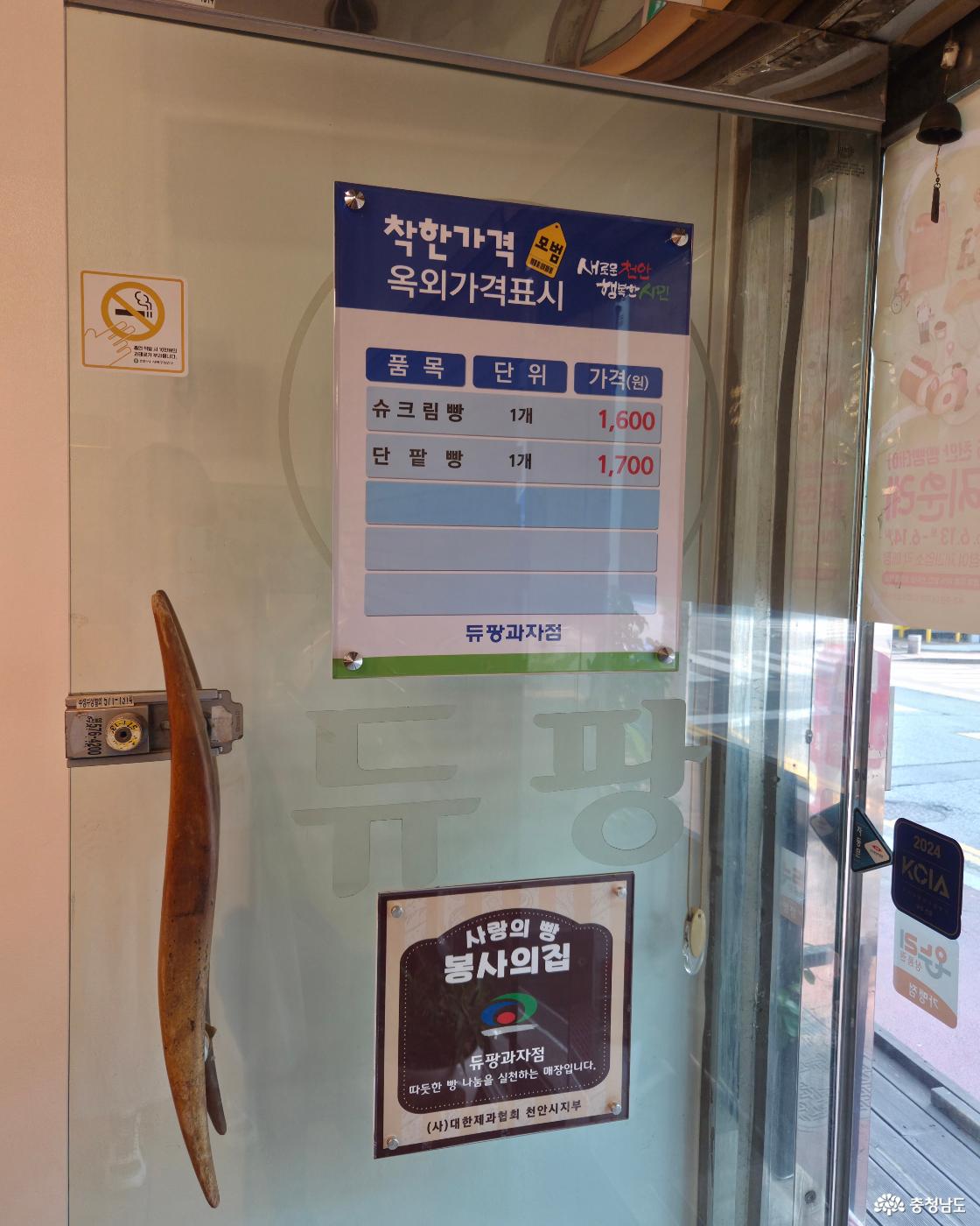 매장 유리문에 착한가격업소 안내문이 부착되어 있습니다. '슈크림빵 1,600원, 단팥빵 1,700원'이 적힌 '착한가격업소 옥외가격표시' 판넬이 부착되어 있습니다. 문 아래쪽에는 따뜻한 나눔을 실천하는 매장임을 알리는 '사랑의 빵 봉사의 집' 문패가 함께 걸려 있습니다.