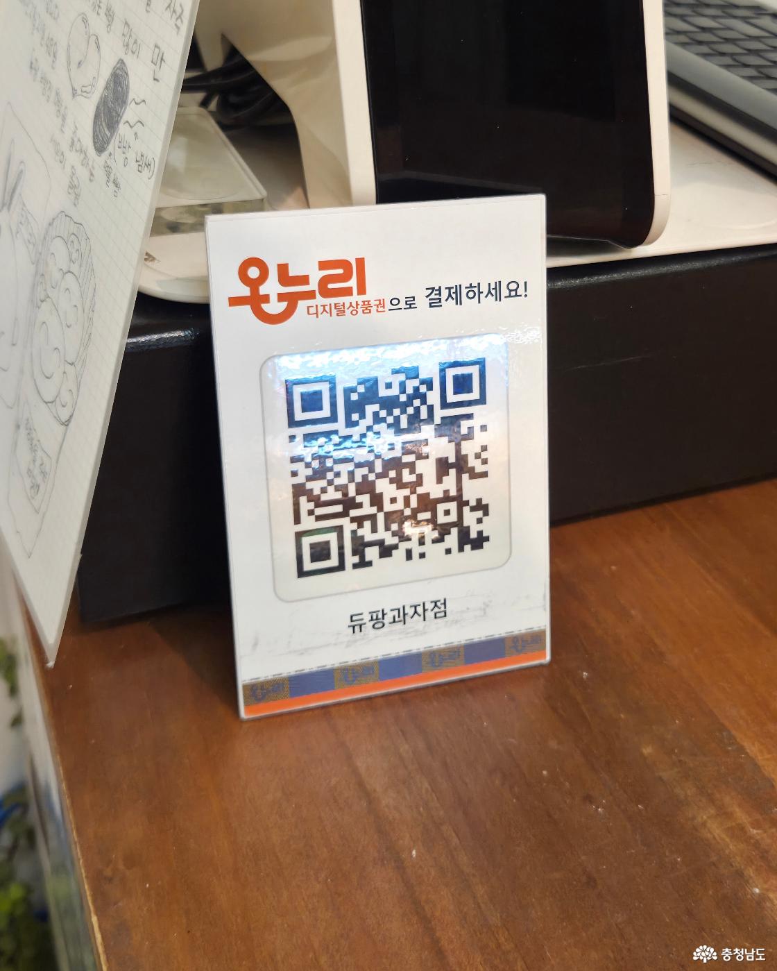 매장 계산대의 나무 테이블 위에 온누리 디지털상품권 결제를 위한 QR코드 안내판이 세워져 있으며, 왼쪽에는 꼬마손님의 아기자기한 손그림이 그려진 편지가 부착되어 있습니다.