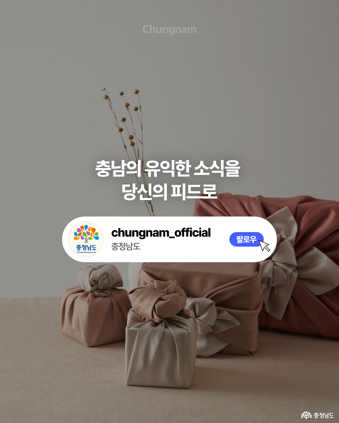 차분한 회색 배경에 분홍색과 베이지색 보자기로 포장한 여러 크기의 선물상자가 놓여 있고, 뒤쪽에는 마른 꽃가지를 꽂은 화병이 배치되어 있습니다. 중앙에는 &lsquo;충남의 유익한 소식을 당신의 피드로&rsquo;라는 문구와 충청남도 공식 계정의 &lsquo;팔로우&rsquo; 버튼이 크게 표시되어 있습니다.