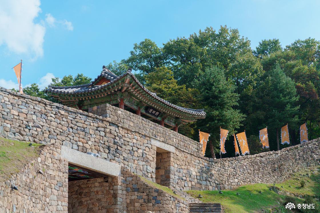 아래쪽에서 올려다본 공산성 금서루와 성벽. 단청을 칠한 문루 아래 성문과 돌계단, 벽을 따라 이어지는 황색 깃발들.
