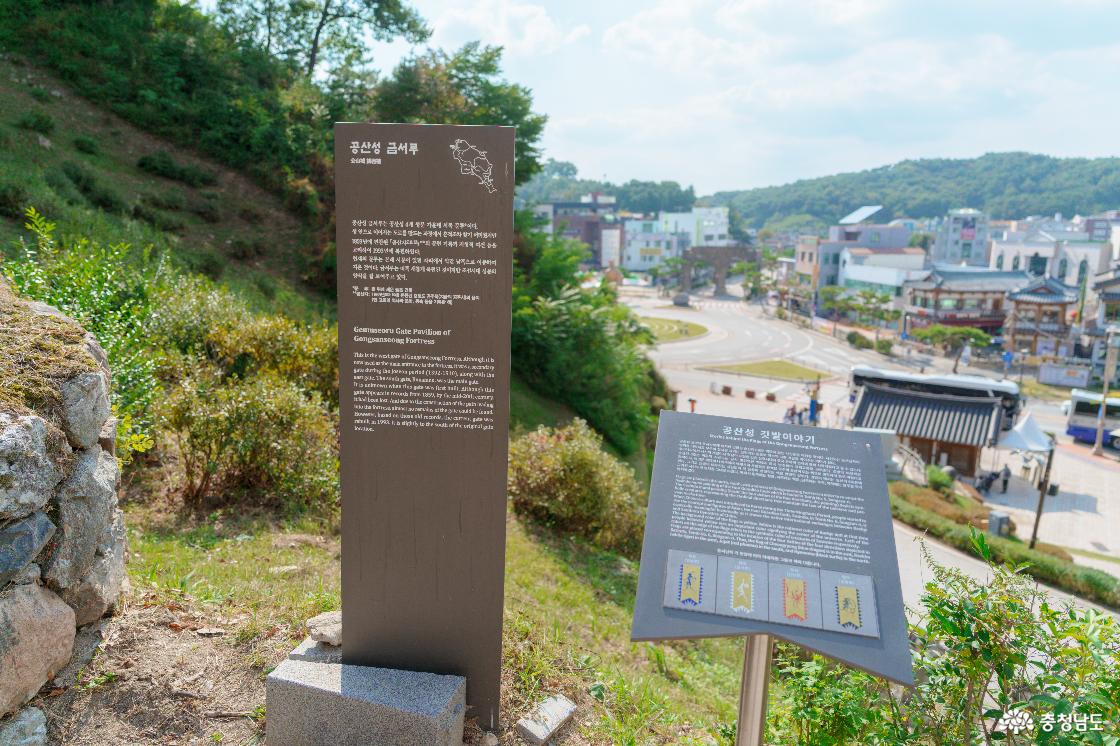 공산성 금서루와 공산성 깃발이야기 안내판. 뒤편 성 아래로 보이는 공주 도심과 원형 교차로, 기와지붕 건물들.