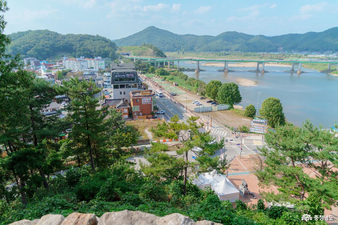 공산성에서 바라본 금강변 공주 시내. 강가를 따라 이어지는 도로와 건물들, 강을 가로지르는 다리와 주변 산.