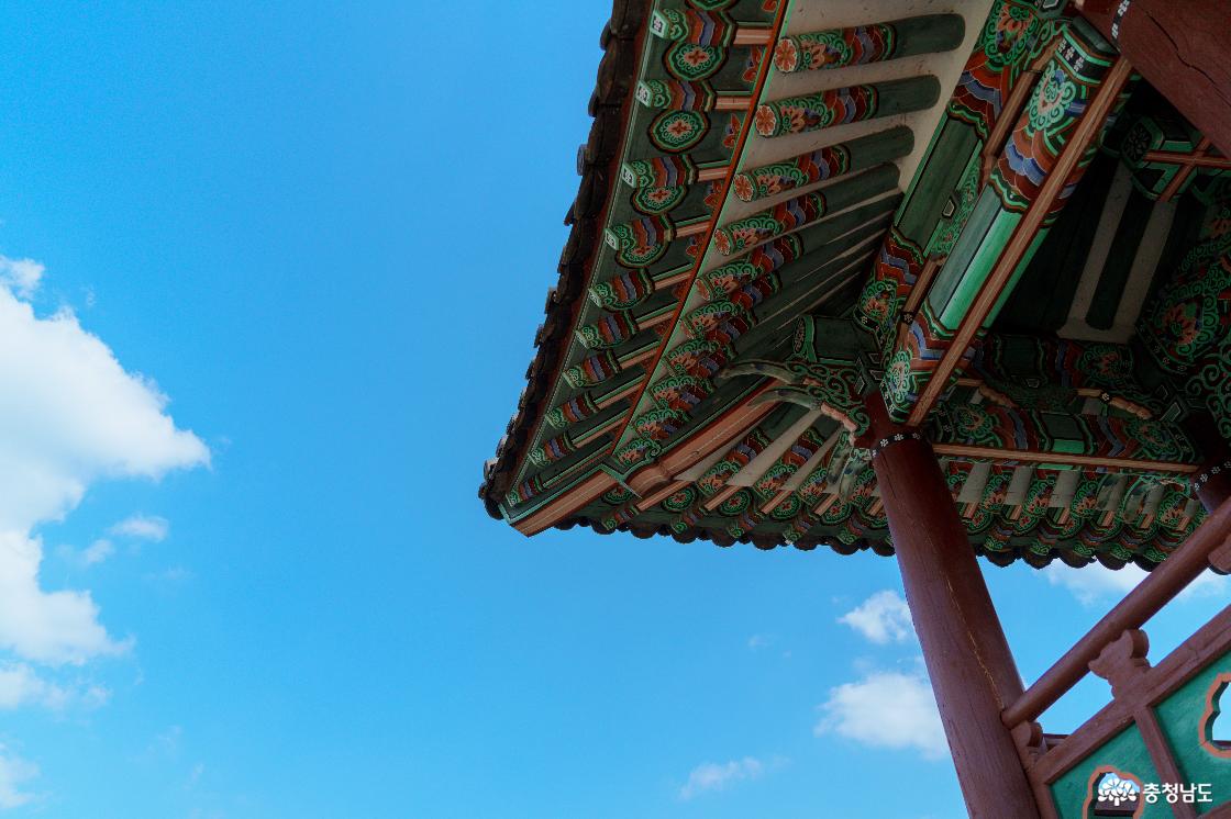 아래에서 올려다본 공산정 처마와 붉은 기둥. 초록·주황·파랑의 꽃무늬 단청과 푸른 하늘.