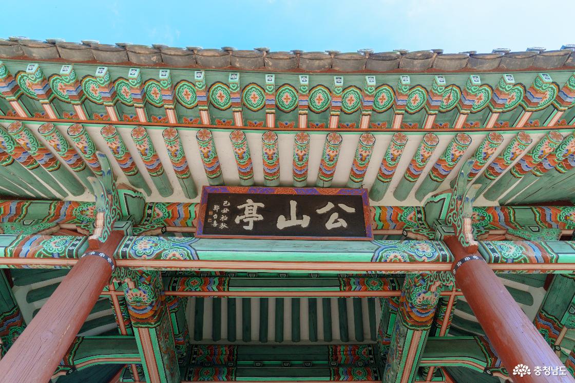 공산정 처마 아래 공산정 한자 현판과 단청. 붉은 기둥 사이 초록색 들보와 꽃무늬로 장식한 서까래.