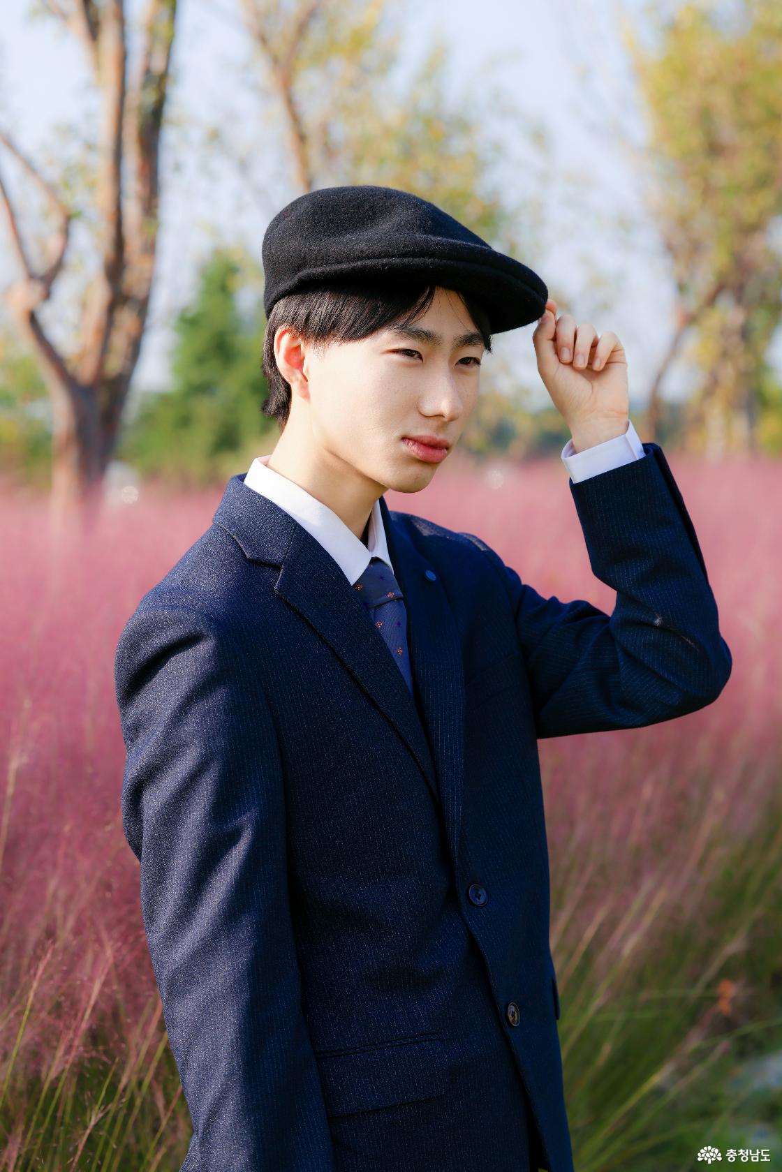 정장 촬영을 선택한 이승민씨(20대)가 핑크뮬리를 배경으로 모자 챙에 손을 얹고 포즈를 취하고 있다.