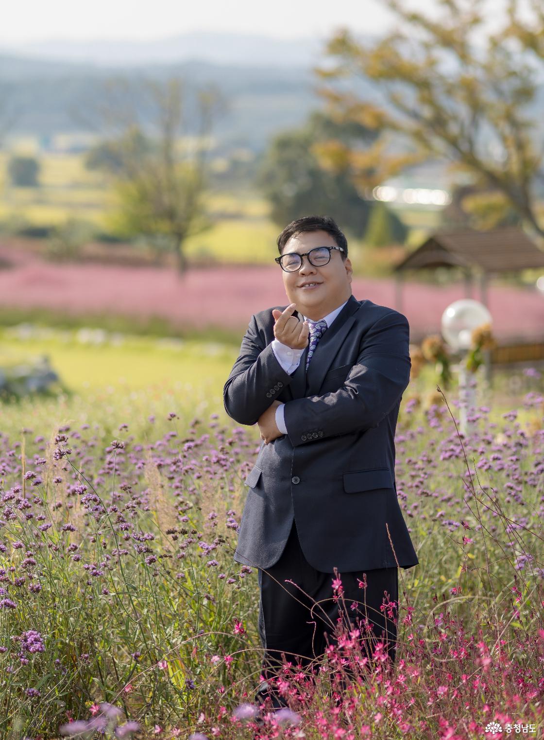 이해만씨(40대)가 정원의 꽃들 사이에서 손가락 하트를 만들며 미소 짓고 있다. 그는 촬영한 사진을 집에 걸어두고 어머니께 보여드리고 싶다고 말했다.