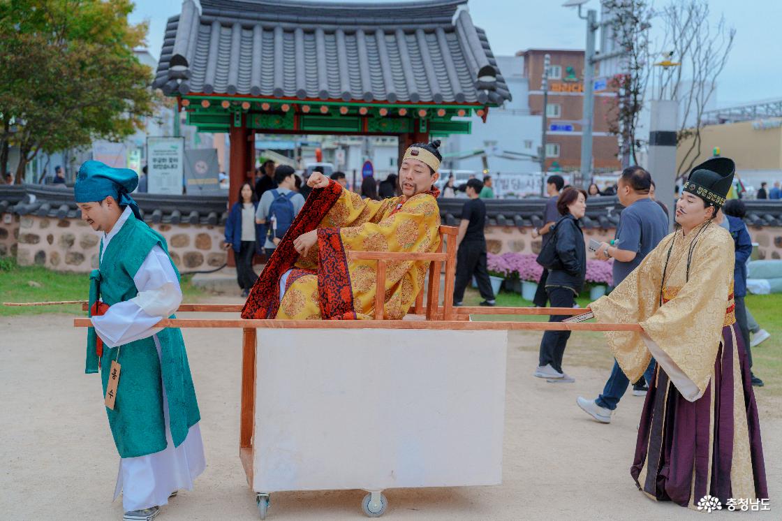 정림사지 입구에서 가마 행렬을 연기하는 백제연희단. 황금색 왕복을 입고 바퀴 달린 가마에 앉은 배우와 앞뒤에서 가마채를 잡은 배우들.