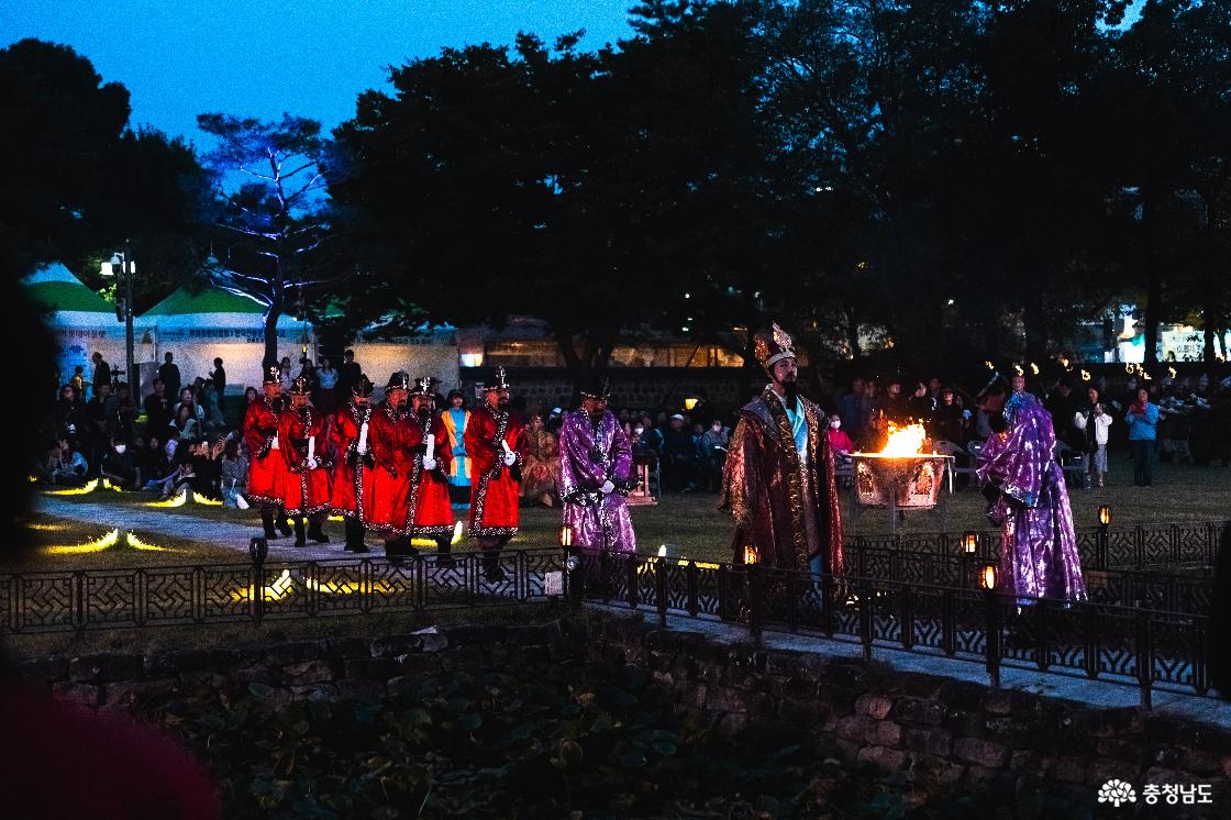 밤의 정림사지에서 왕의 행차를 재현하는 사비천도선포식 출연진. 관과 왕복을 입은 인물을 앞세워 보라색 관복과 붉은 군복 차림의 행렬이 이동하는 모습.