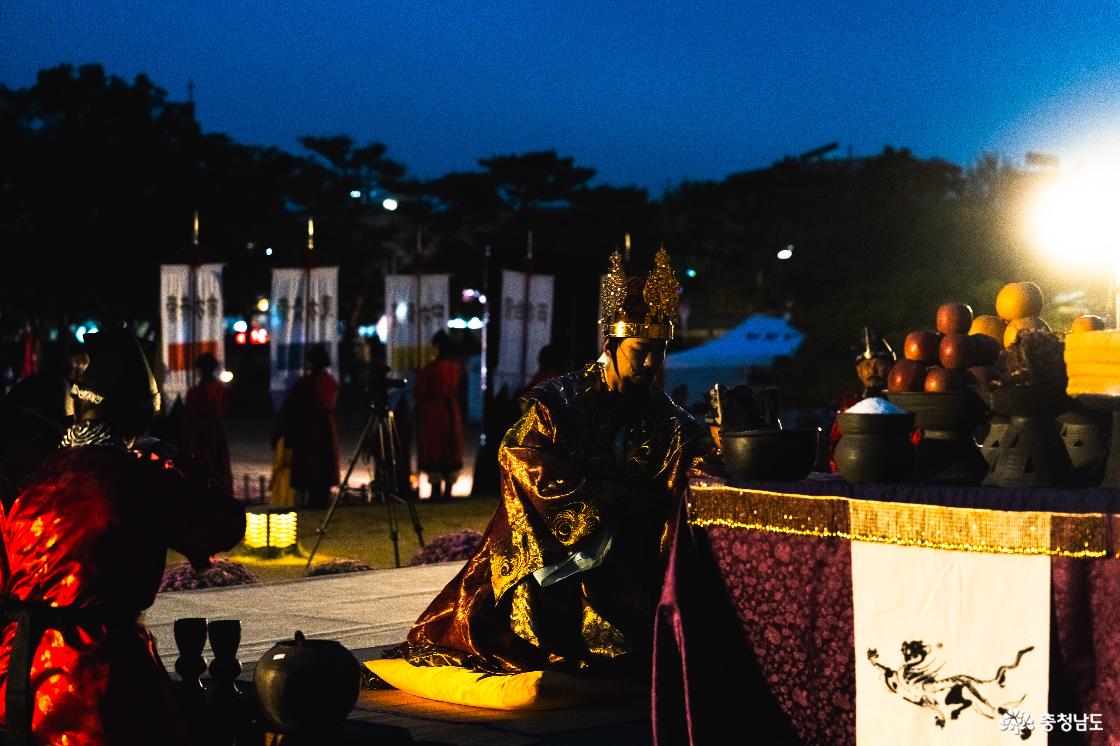 사비천도선포식 제단 앞 노란 방석에 무릎을 꿇고 의식을 치르는 왕 역할의 출연자. 금빛 관과 왕복, 제단 위 과일과 제기.