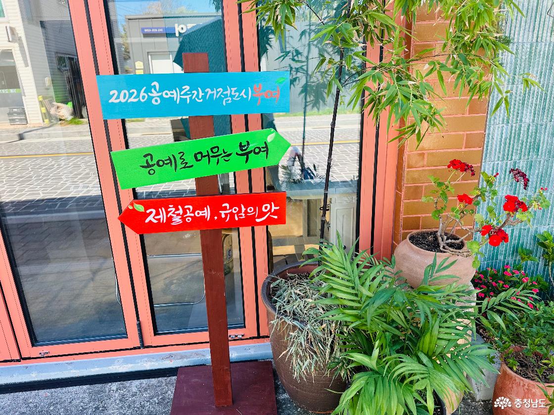 규암마을 건물 앞 화분 옆에 세워진 색색의 안내 표지판. 2026 동아시아문화도시 부여, 공예로 머무는 부여, 제철공예·규암의 맛 문구.