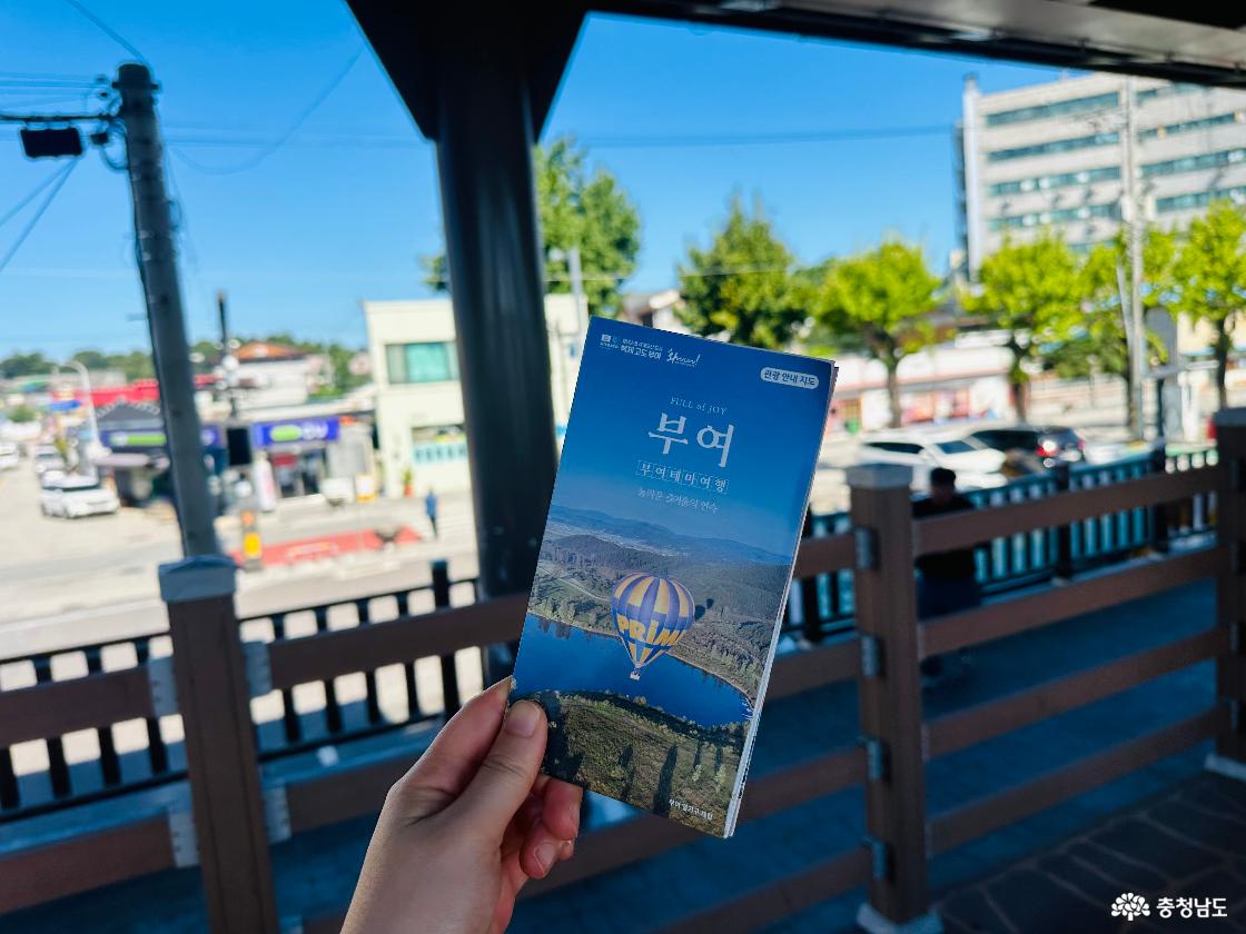 규암마을 거리와 나무 난간을 배경으로 손에 든 부여 관광안내지도. 표지에 강과 열기구 사진이 실린 안내책자.