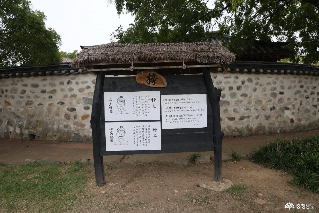 돌담 앞 초가지붕 게시판에 붙은 인물 그림과 한문으로 적힌 방